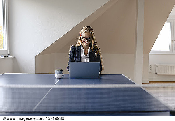 Young businesswoman using laptop on table tennis table in office