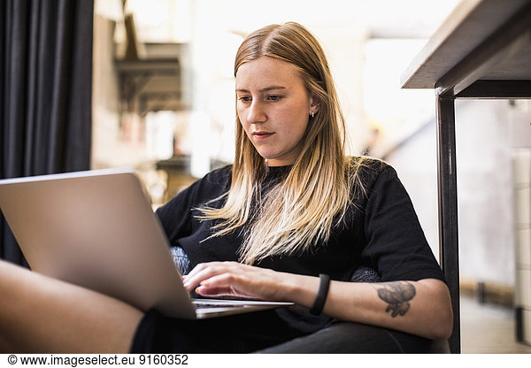 Young businesswoman using laptop while sitting on bean bag in small office