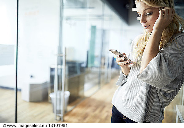 Young businesswoman using mobile phone while standing at corridor