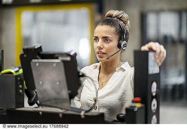 Young businesswoman wearing headset operating machine in factory