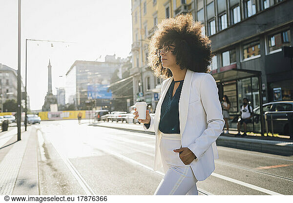 Young businesswoman with coffee cup walking in city