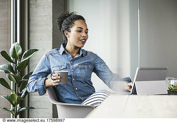 Young businesswoman with coffee cup working on tablet computer in office