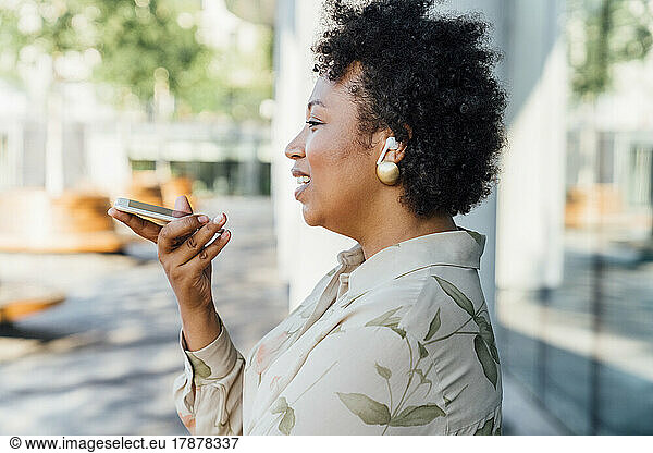 Young businesswoman with curly hair talking on mobile phone through speaker