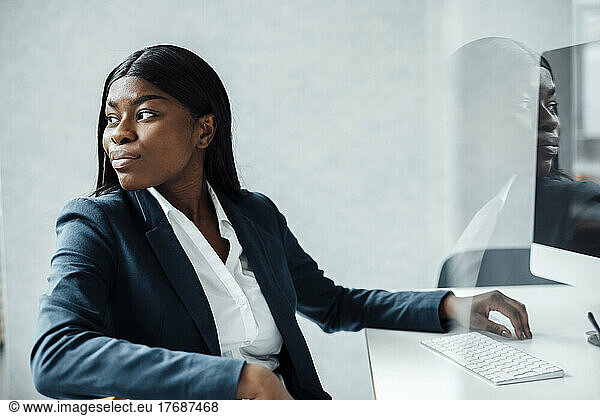 Young businesswoman with desktop PC at desk seen through glass