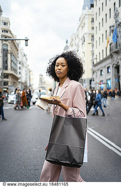 Young businesswoman with food and shopping bag walking on street