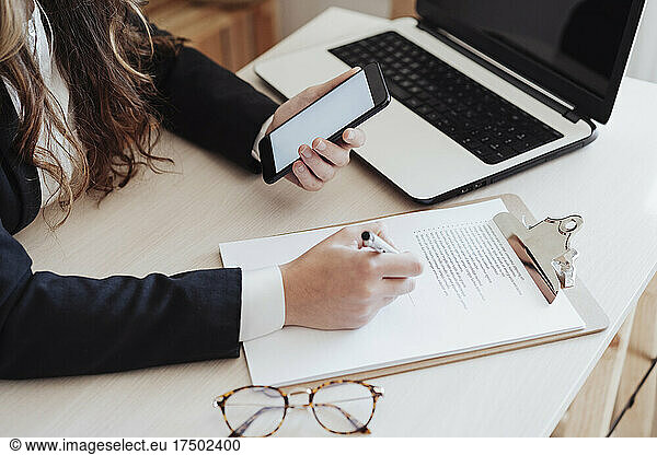 Young businesswoman with smart phone filling in form at office