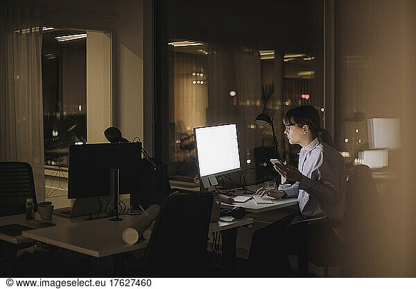 Young businesswoman with smart phone using computer at work place