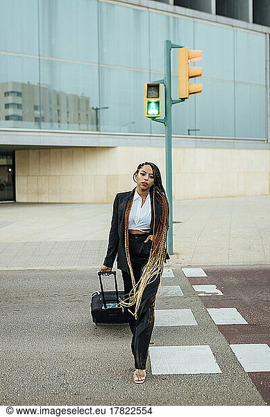 Young businesswoman with suitcase crossing street