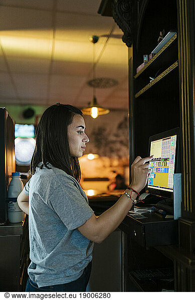 Young cashier operating touch screen computer at bar