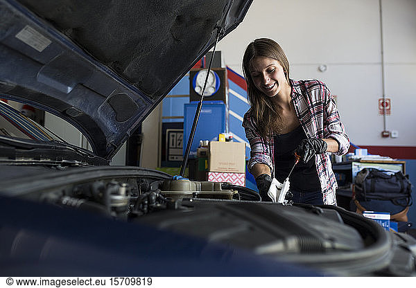 Young casual woman in shirt and gloves working with car in repair service checking engine oil level