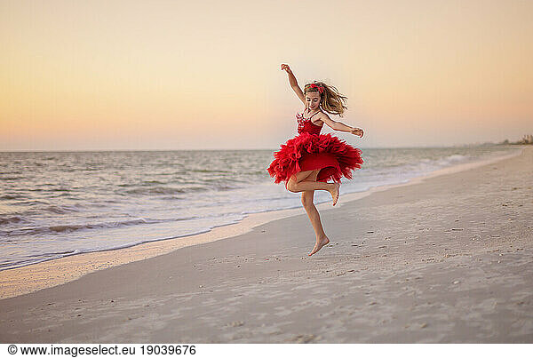 Young Caucasian Girl dancing and twirling on beach in a red dress