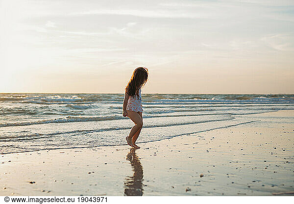 Young caucasian girl on the beach at sunset walks in the low tide