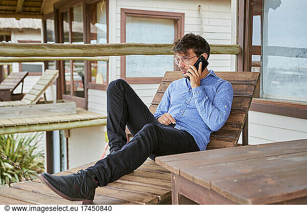 Young caucasian man talking on his smartphone resting on his balcony