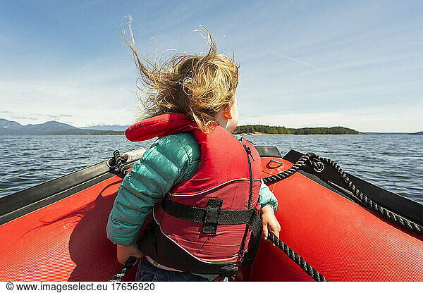Young child sits on bow of rubber raft in big sunny bay