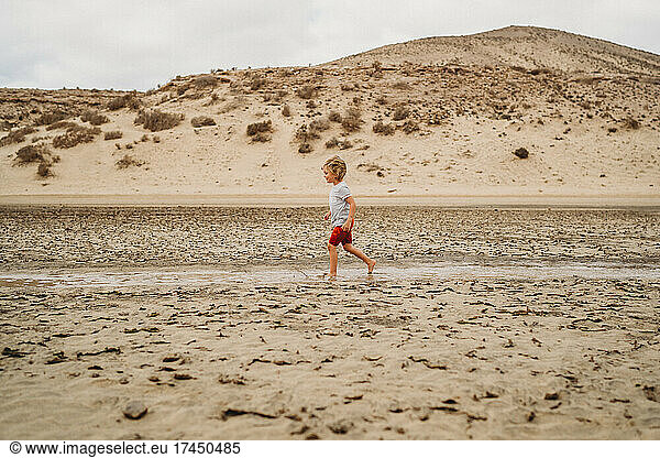 Young child walking between sand dunes at beach on cloudy day