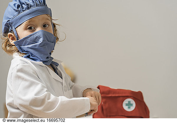 young child wearing medical PPE turns to look directly at viewer as medical bag sits in the background