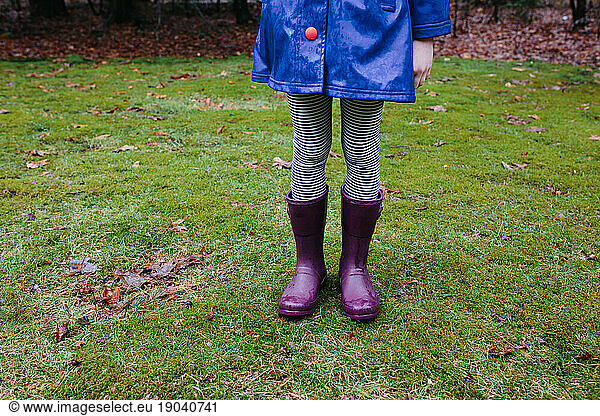 Young child wearing purple rain boots in a wet  mossy forest
