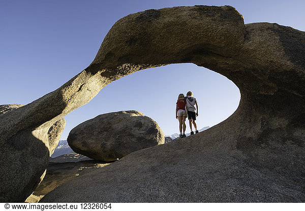 Young children standing under a natural rock arch  Alabama Hills; California  United States of America