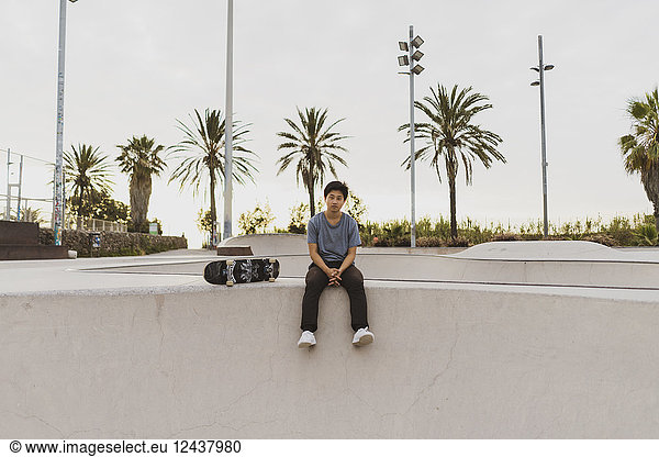 Young Chinese man sitting on wall of a skate park near the beach