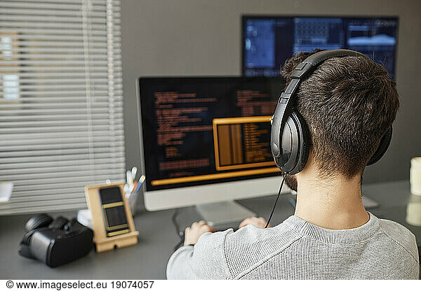 Young computer programmer wearing headphones working on desktop PC