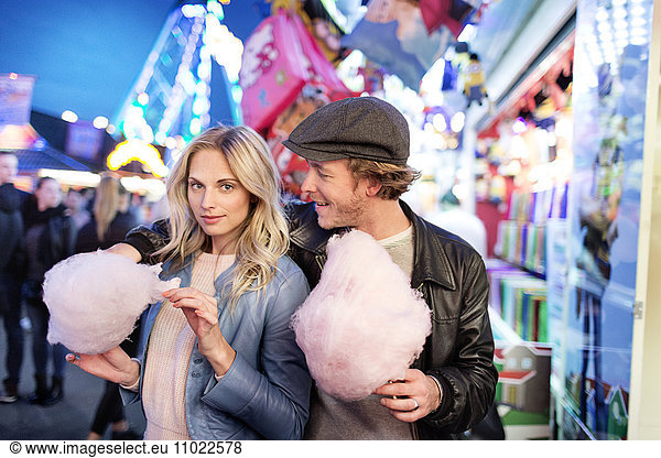 Young couple at fun fair eating candy floss