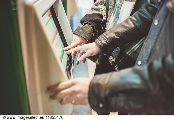 Young couple buying train tickets using touchscreen ticket machine