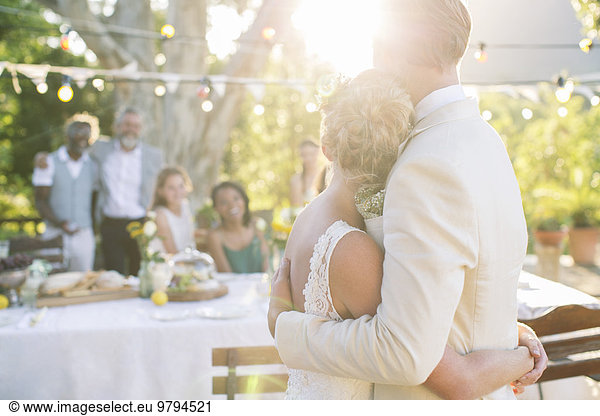 Young couple embracing in garden during wedding reception
