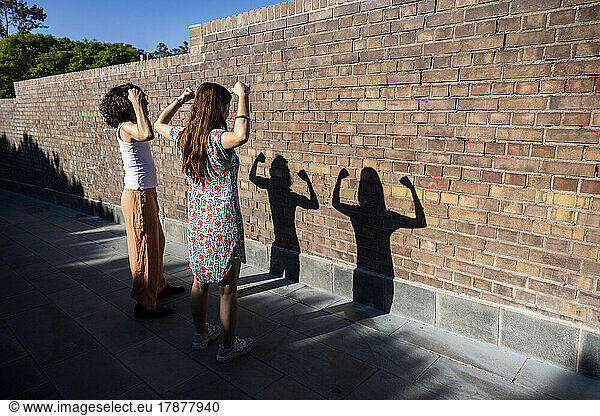 Young couple flexing muscles in front of wall on sunny day