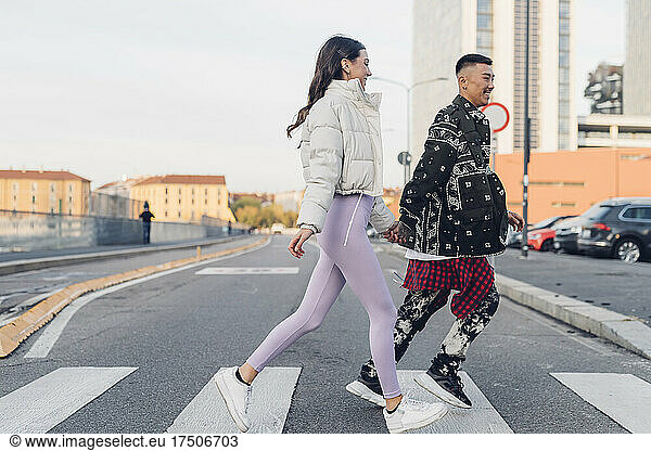 Young couple holding hands and crossing street in city
