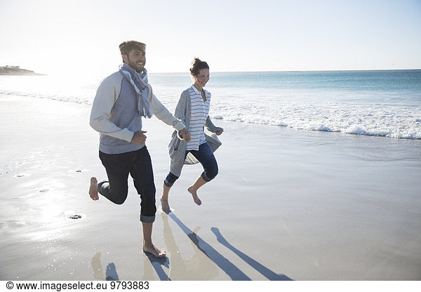 Young couple holding hands and running on beach