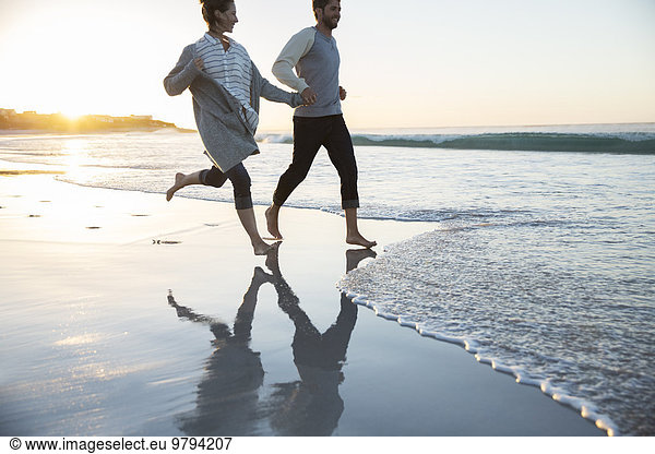 Young couple holding hands and running on beach