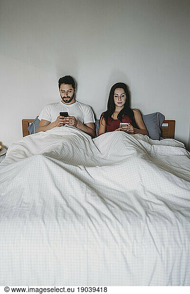 Young couple in bed looking at their smartphones