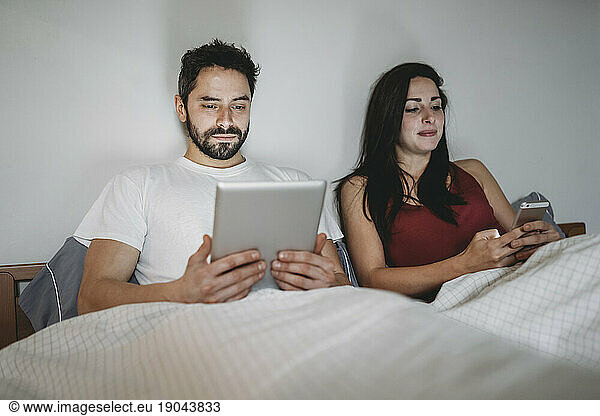 Young couple in bed using the smartphone and the tablet