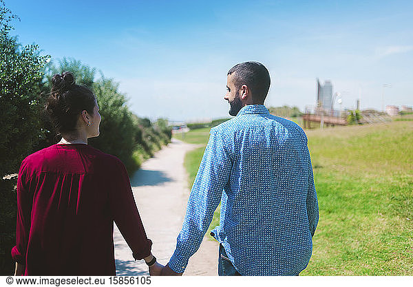 Young couple in casual wear walking away with hand in hand at sunset