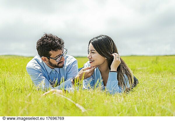 Young couple in love lying on the grass touching each other's faces  two people in love lying on the grass looking at each other  A couple lying on the grass looking at each other