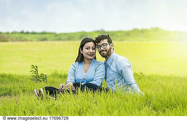 Young couple in love sitting on the grass looking at the camera  Two lovers sitting on the grass looking at the camera  Portrait of a couple in love sitting on the grass in the field