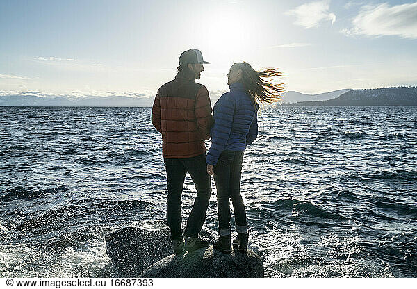 Young couple in love stand on rock in Lake Tahoe in the winter