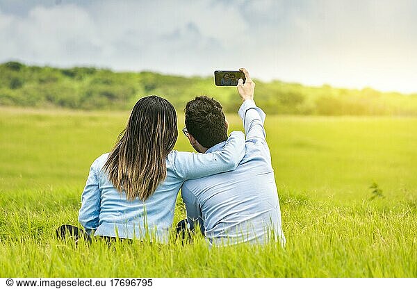 Young couple in love taking a selfie in the field  People in love taking selfies in the field with their smartphone  Smiling couple in love sitting on the grass taking selfies
