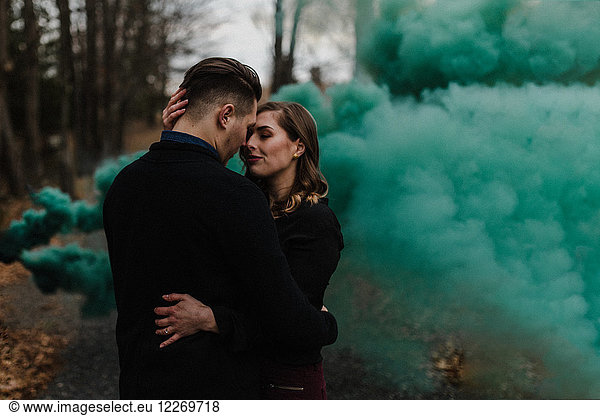 Young couple kissing in forest by green smoke cloud