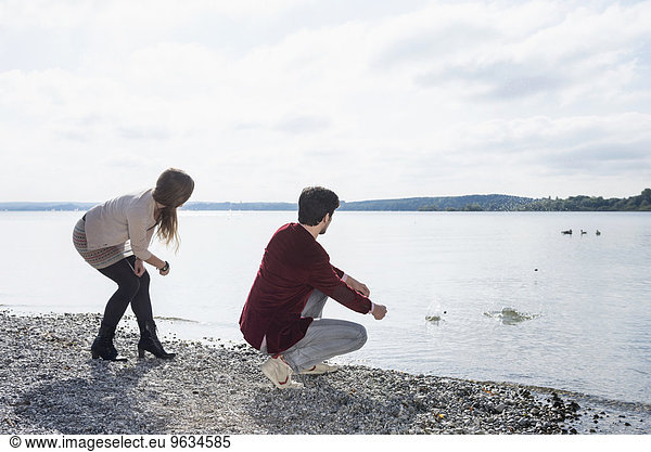 Young couple lake skimming stones