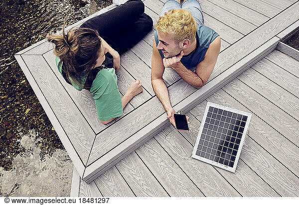 Young couple lying on patio charging mobile phone through solar energy