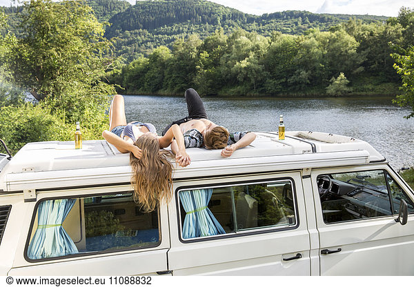 Young couple lying on roof of a van at lakeside