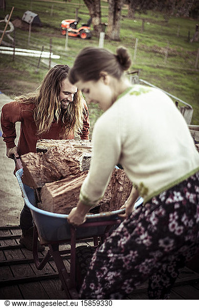 young couple man and woman stack wood in wheelbarrow on farm