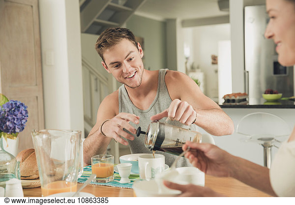 Young couple pouring breakfast coffee at kitchen table