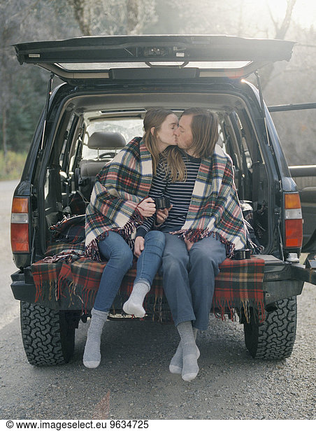 Young couple sitting in the back of their car  kissing.