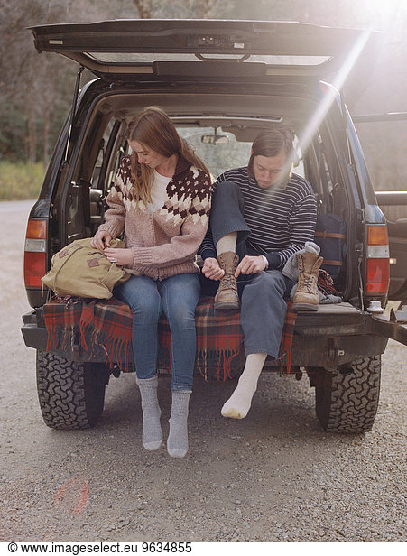 Young couple sitting in the back of their car  putting on boots.