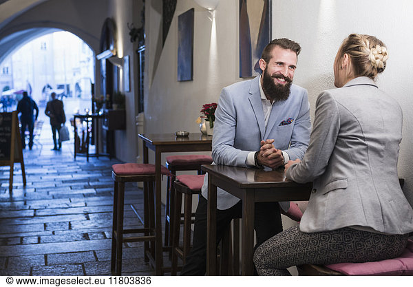 Young couple sitting on stool and talking at sidewalk cafe