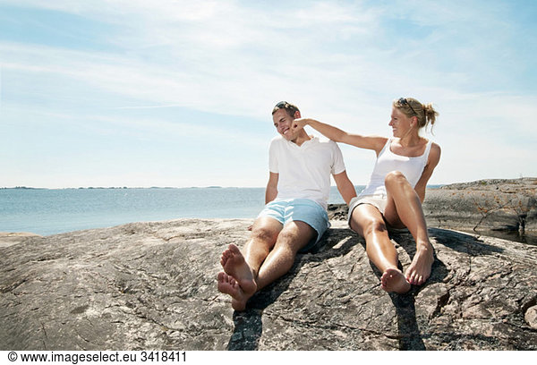Young couple sitting on the rock by the water