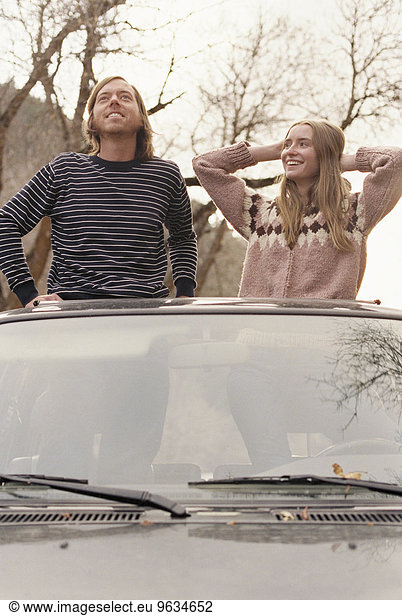 Young couple standing in their car  looking through sunroof.