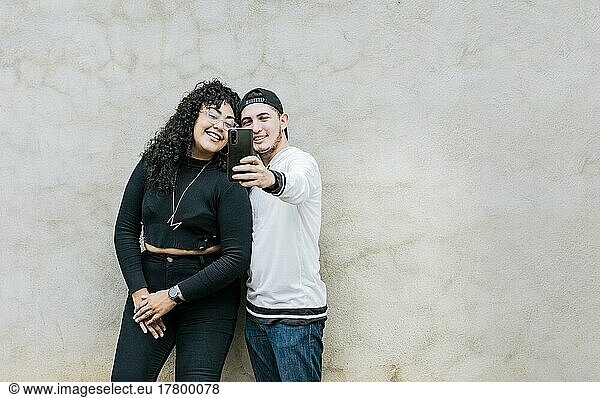 Young couple taking a selfie near a wall with copy space  Young friends taking a selfie leaning against a wall  Young happy couple taking a selfie leaning against a wall